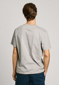 Medvilninis marškinėlis trumpomis rankovėmis, su horizontaliomis šviesiai mėlynomis juostelėmis ant nuobodaus smėlio fono. Paprastas apvalus kaklo iškirpimas.