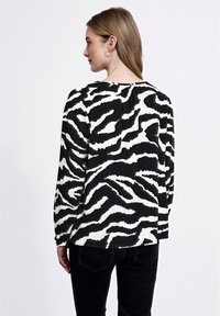 Maglietta a maniche lunghe bianca e nera con un motivo a zebre ondulate, con una vestibilità comoda e un tessuto morbido, vista da dietro.