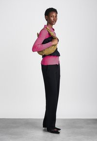 Roosa pika varrukaga kardigan musta volangilise pluusi peal, kombineeritud mustade pükste ja terava ninaga kingadega. Hoides mustrinäitega sinepikollast kotti.