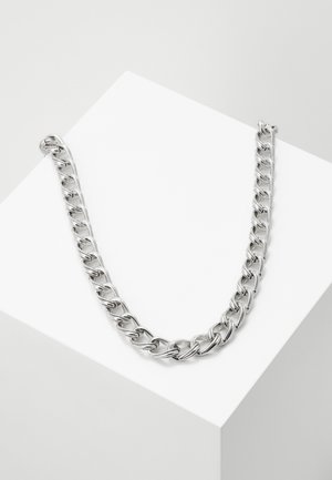 Collier épais en chaîne argentée avec des maillons ovales entrelacés, présenté sur une surface blanche inclinée.