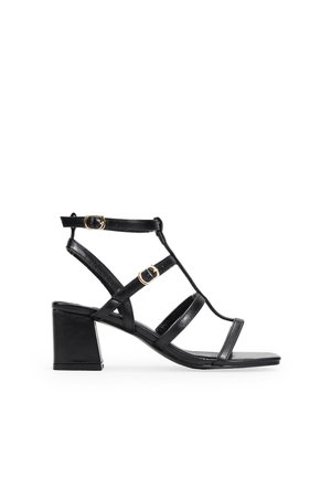 Sandalias negras de tacón con puntera abierta, que cuentan con tiras delgadas, acentos de metal dorado y un diseño de tacón cuadrado.