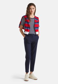 Námořnické kalhoty spojené s červeno-bílým proužkovaným tričkem s krátkým rukávem a červeným pruhovaným svetr přehoděným přes ramena. Béžové tenisky.