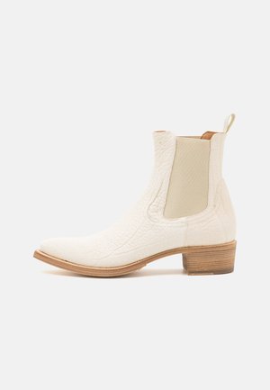 Białe skórzane botki za kostkę o teksturowanej powierzchni, z elastycznymi panelami bocznymi i niskim drewnianym obcasem. Zawierają pętelkę z tyłu ułatwiającą zakładanie.