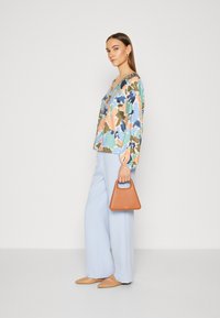 Blusa floreale multicolore, pantaloni ampi azzurri, ballerine beige a punta e una piccola borsa marrone con manico.