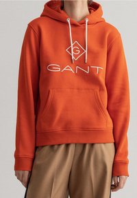 Sweat à capuche en coton orange avec poche kangourou, cordons de serrage et logo blanc en forme de losange. Poignets et ourlet côtelés pour un ajustement parfait.