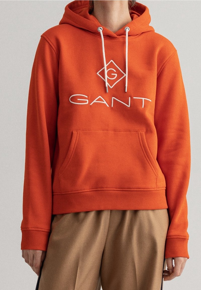 Sweat à capuche en coton orange avec poche kangourou, cordons de serrage et logo blanc en forme de losange. Poignets et ourlet côtelés pour un ajustement parfait.