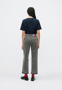 Tmavomodré bavlnené tričko v kombinácii so sivými džínsami s vysokým pásom a neupraveným lemom, červenými ponožkami a čiernymi topánkami s lesklým povrchom.