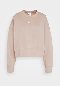 Ljusbeige kort sweatshirt i mjukt tyg, med rund halsringning och långa, avslappnade ärmar. Nike-logotyp i guld på bröstet.