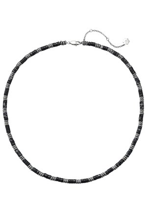Frau trägt eine schwarz-silberne Perlenkette, silbernen Creolen-Ohrring und ein trägerloses Oberteil mit pinkem, grünem und weißem geometrischem Muster.