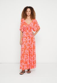 Ziedu maxi kleita dzīvīgos oranžās un rozā toņos, ar V veida izgriezumu, savāktu vidukli, īsām plīvurojuma piedurknēm un plūstošu siluetu.