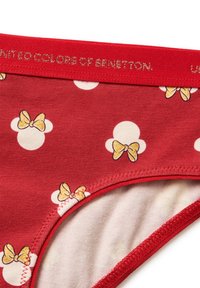 Červené spodní prádlo s bílými puntíky, na kterém jsou motivy hlav Minnie Mouse s žlutými mašlemi a červeným pasem s nápisem "United Colors of Benetton".