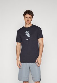 T-shirt de algodão azul-marinho com um logotipo branco "Sox" e o swoosh da Nike, combinado com calções cinza-claro. Design simples e decote redondo.