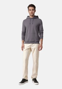 Sweat à capuche gris avec une poche avant, associé à un pantalon crème et des baskets noires. Tissu doux, coupe décontractée et design simple.