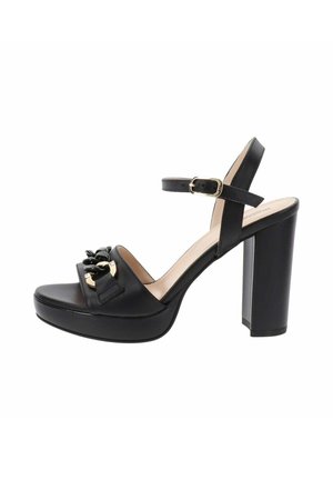 Sandal alto nero con tacco, con cinturino alla caviglia, suola a piattaforma, texture in pelle liscia, dettagli in hardware dorato e fiocco decorativo.