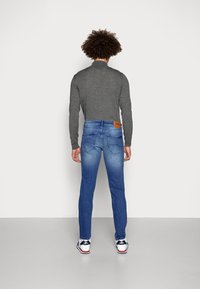 Šedé tričko s dlouhým rukávem, modré džíny s vybledlým designem a zadními kapsami, a tenisky v námořnické modré a bílé barvě.