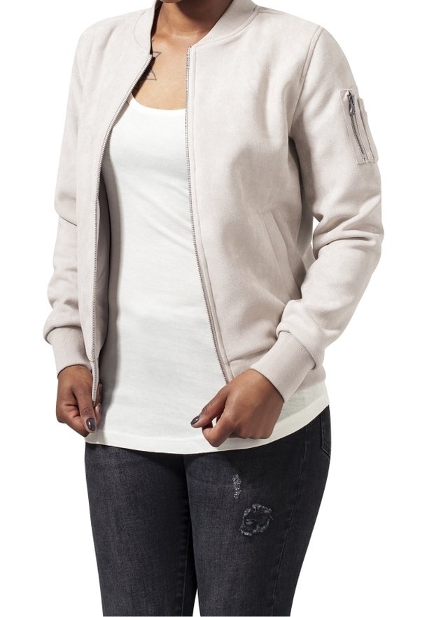 Personne portant une veste bomber beige clair sur un débardeur blanc et un jean sombre usé, mains ajustant la fermeture éclair de la veste.