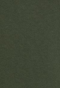 Gros plan sur un tissu tricoté vert olive montrant la texture détaillée des mailles et un motif uniforme.