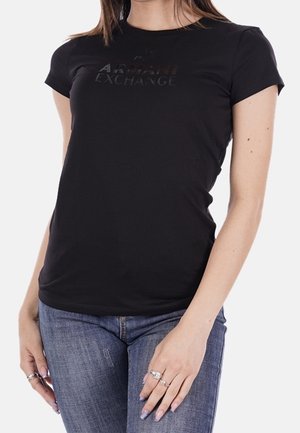 Mujer que lleva una camiseta negra ajustada de Armani Exchange y vaqueros azules, con anillos en los dedos y esmalte de uñas lila claro.