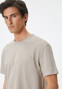 Lys beige bomulds T-shirt med rund halsudskæring, korte ærmer og en brystlomme. Glat tekstur og standard pasform.