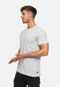 Graues Baumwoll-T-Shirt, Rundhalsausschnitt, kurze Ärmel, mit kleinem Logo auf der Brust und einem Etikett an der unteren linken Seite.