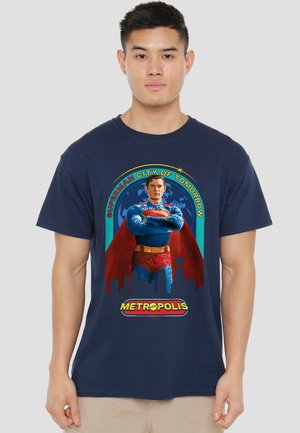 Young man wearing navy blue t-shirt with colorful Superman graphic and text "Superman City of Tomorrow" and "Metropolis" on front.