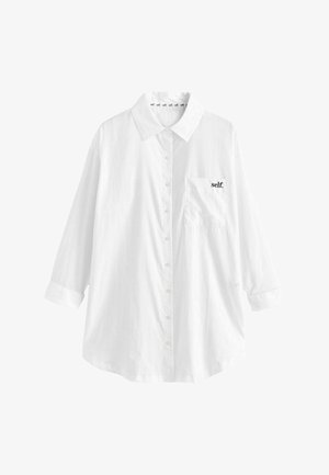 Balta marškinėliai su apykakle, ilgomis rankovėmis ir priekinėmis kišenėmis, dekoruoti juodu "self." siuvinėjimu. Minkšta medžiaga su lygiu paviršiumi.