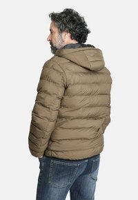 Chaqueta de plumas marrón con capucha, que presenta una textura acolchada y un diseño ajustado. Combinada con jeans de mezclilla azul.