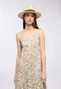 Vestito beige a fantasia con spalline sottili e gonna a strati, con bottoni davanti. Il modello indossa un cappello di paglia a tesa larga con un nastro nero.