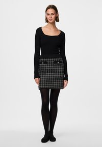 Top a maniche lunghe nero a costine abbinato a una gonna corta a quadri con accenti bianchi e due tasche frontali, indossato con collant neri e ballerine.