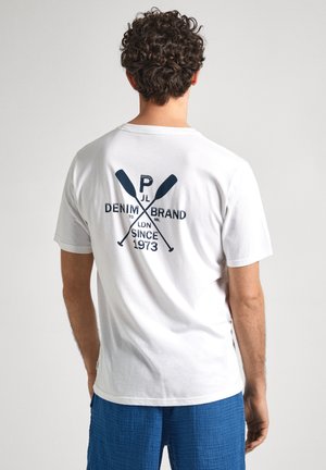 Camiseta de algodón blanca con un diseño gráfico azul en la parte trasera que presenta palas cruzadas y texto. Manga corta y diseño de cuello redondo.