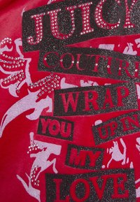 Červená fleecová látka s čiernymi a trblietavými písmenami s kamienkami. Text obsahuje "JUICY COUTURE" a frázy v rôznych typoch písma a veľkostiach.