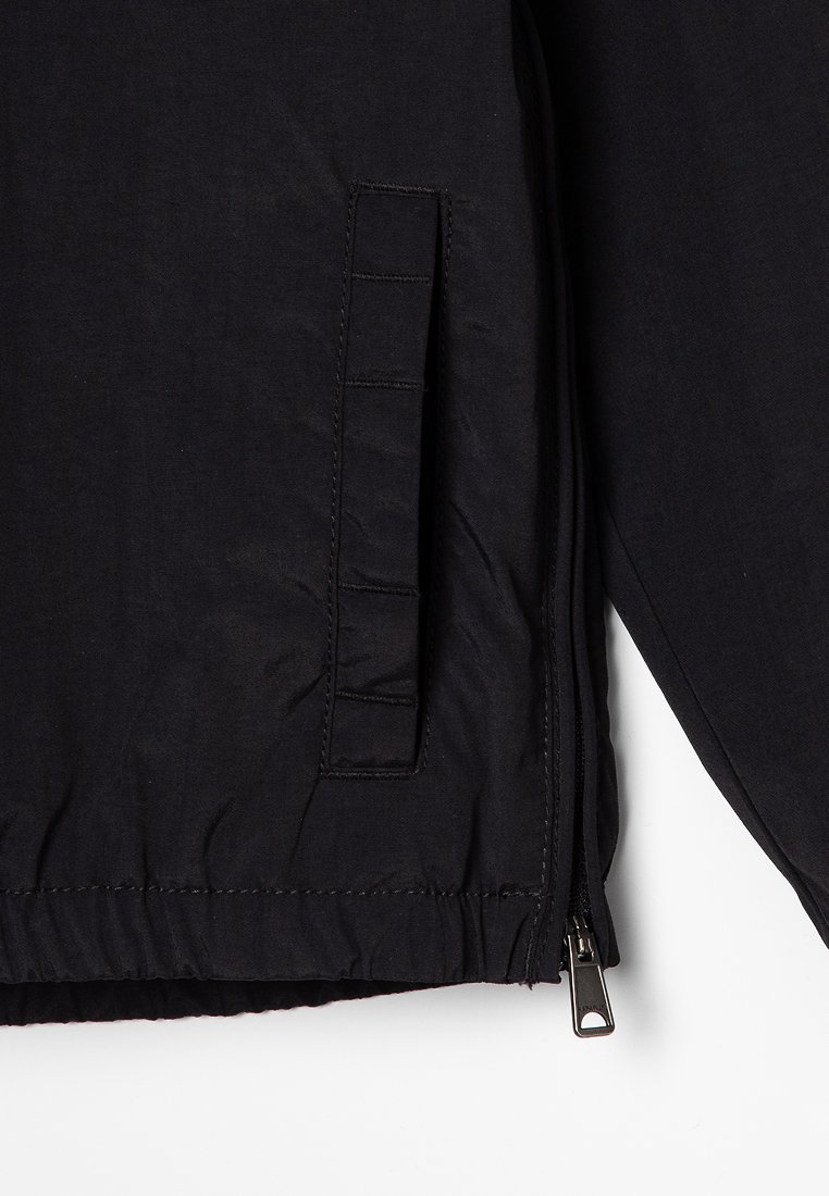 Giacca nera imbottita con chiusura a zip, tasca laterale con dettagli di cucitura e una texture liscia, leggermente stropicciata.