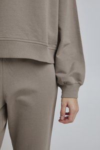 Pullover color marrone chiaro con polsini e orlo a costine, caratterizzato da una vestibilità comoda. Abbinato a pantaloni color marrone chiaro coordinati. Tessuto morbido.