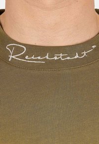 T-shirt in cotone verde oliva con texture a coste e colletto rotondo. Presenta il nome del marchio ricamato in bianco sul collo.
