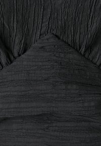 Tessuto nero con superficie texturizzata caratterizzata da ondulazioni verticali e orizzontali. Design sartoriale con un dettaglio appuntito al centro.