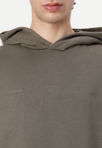 Olive green hoodie with a texture feel, featuring a drawstring hood and embossed logos on the chest and sleeve. Simple design.
