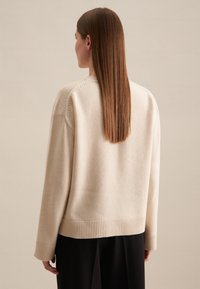 Beige gebreide trui met een losse pasvorm, geribde manchetten en zoom, met een brede halslijn en minimale stikdetails.