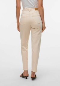 Beige høytlivsjeans med slim fit, med baklommer og et brunt lærmerke på midjebåndet. Glatt stoffstruktur.