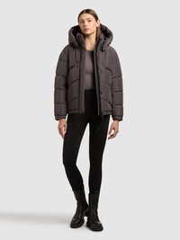 Szara ocieplana kurtka z kapturem, z zamkiem z przodu, bocznymi kieszeniami i pikowaną strukturą. W komplecie z czarnymi legginsami i botkami za kostkę.