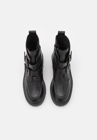 Paire de bottines en cuir noir avec double brides à boucle et semelles en caoutchouc épaisses, vues de dessus sur un fond blanc.