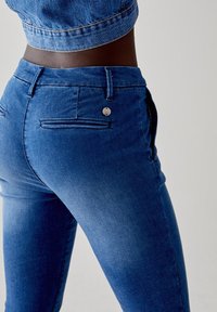 Jeans skinny in denim blu caratterizzati da un classico design a cinque tasche, texture liscia e un singolo bottone frontale con un accento metallico.