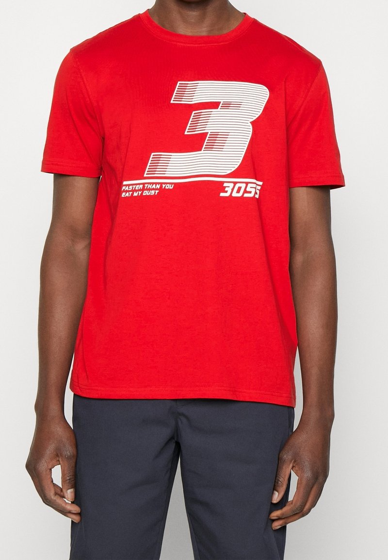 Homme portant un T-shirt rouge avec un grand numéro blanc 3 et le texte "Faster than you eat my dust 3055."