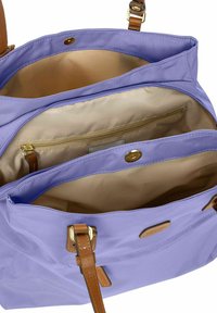 Borsa a spalla lavanda con accenti in pelle marrone, dotata di un ampio interno, tasca con zip e chiusura a scatto. Texture liscia e forma strutturata.