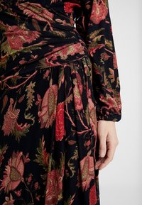 Kukallinen mekko tummansinisellä taustalla, jossa on punaista ja vihreää kirjontaa, poimutettuja yksityiskohtia ja pitkät, elastiset hihat.