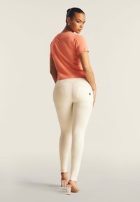 Top pescozzo a maniche corte con scollatura rotonda, abbinato a leggings bianchi aderenti e tacchi trasparenti. Dettagli notevoli nella tasca posteriore.