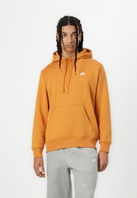 Moletom laranja feito de um tecido suave, com um bolso frontal e capuz ajustável com cordão. Apresenta o logótipo branco da Nike no peito.