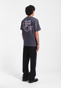 Grå bomullströja med korta ärmar har en grafisk tryck på baksidan som föreställer en taco, drycker och text. Kombinationen med svarta byxor.