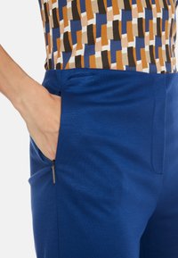 Blue pants featuring a smooth texture and a slim fit, with zipper side pockets and a high waistband, paired with a patterned top.