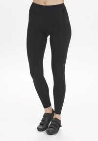 Black cycling leggings with a high waistband, featuring a circular cutout detail and stitched seams. Paired with black cycling shoes.