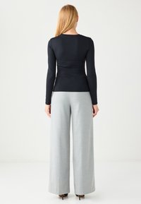 Schwarzes Langarmoberteil mit tailliertem Schnitt, kombiniert mit hochtaillierten, weitgeschnittenen grauen Hosen. Glatte Textur, minimalistisches Design.